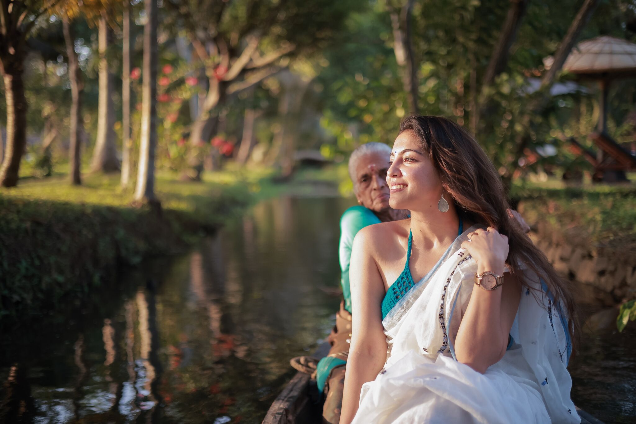 A woman in a white dress sitting on a boat in a park with trees and a pond.
