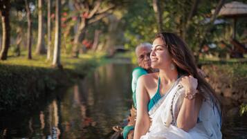 A woman in a white dress sitting on a boat in a park with trees and a pond.