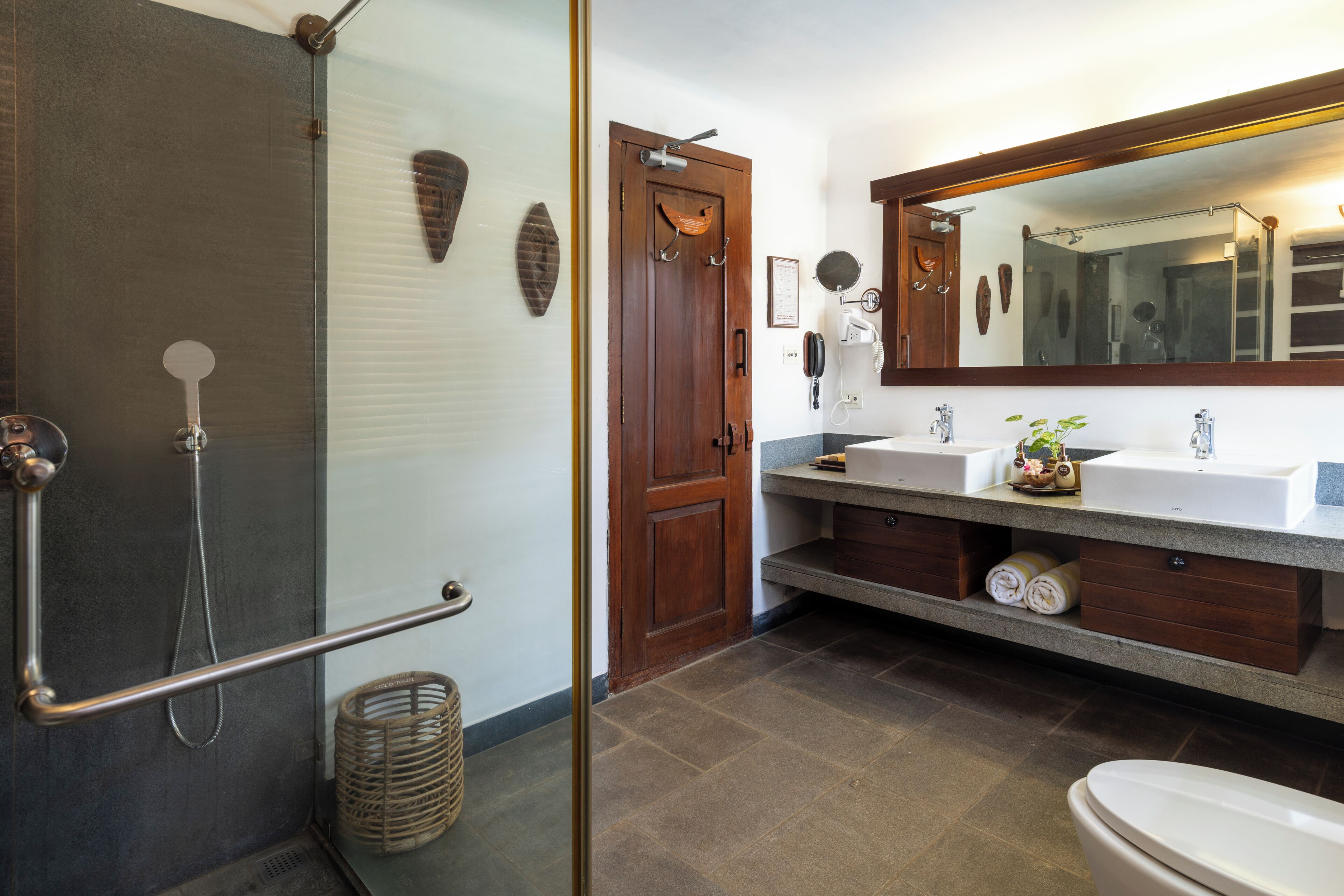 A bathroom with a shower, two sinks, a toilet, a large mirror, and a wooden door.
