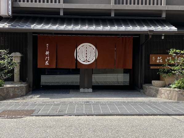 A building entrance with a traditional Japanese design, featuring a tiled roof and a large emblem in the center. - Gion Shinmonso (Kyoto)