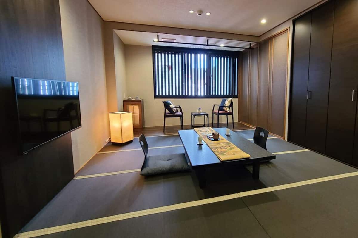 Een kamer met tatami vloerbedekking, een lage tafel met kussens, een televisie en schuifdeuren.