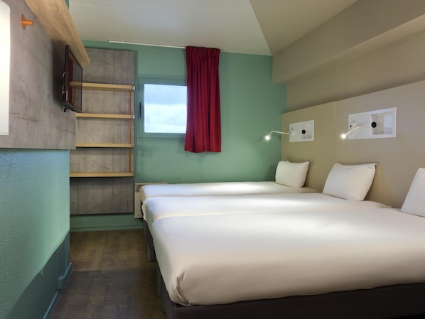 Ein Hotelzimmer mit zwei Betten, einem Fenster mit roten Vorhängen, einem Wand-Fernseher und einer Wandleuchte.
