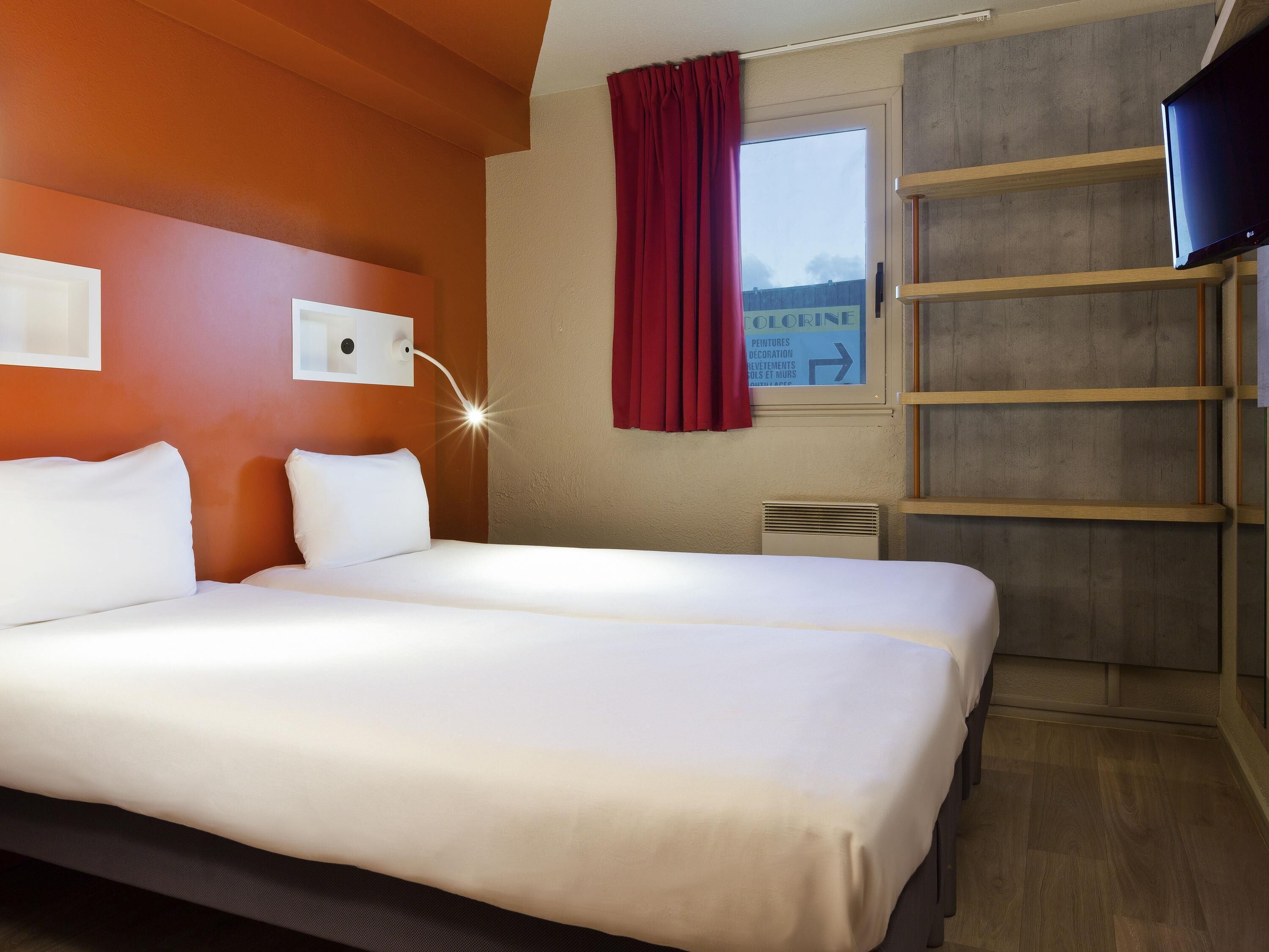 Ein Hotelzimmer mit einem großen Bett, einem Fernseher, einem Fenster mit rotem Vorhang und einem Schild an der Wand.