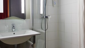 Een moderne badkamer met een douche met glazen wand, een witte wastafel en een spiegel erboven.