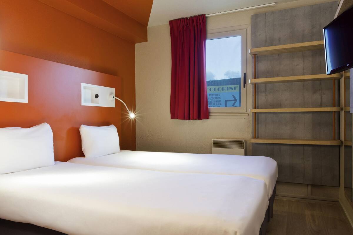 Ett hotellrum med en stor säng, en tv, ett fönster med en röd gardin och en skylt på väggen.