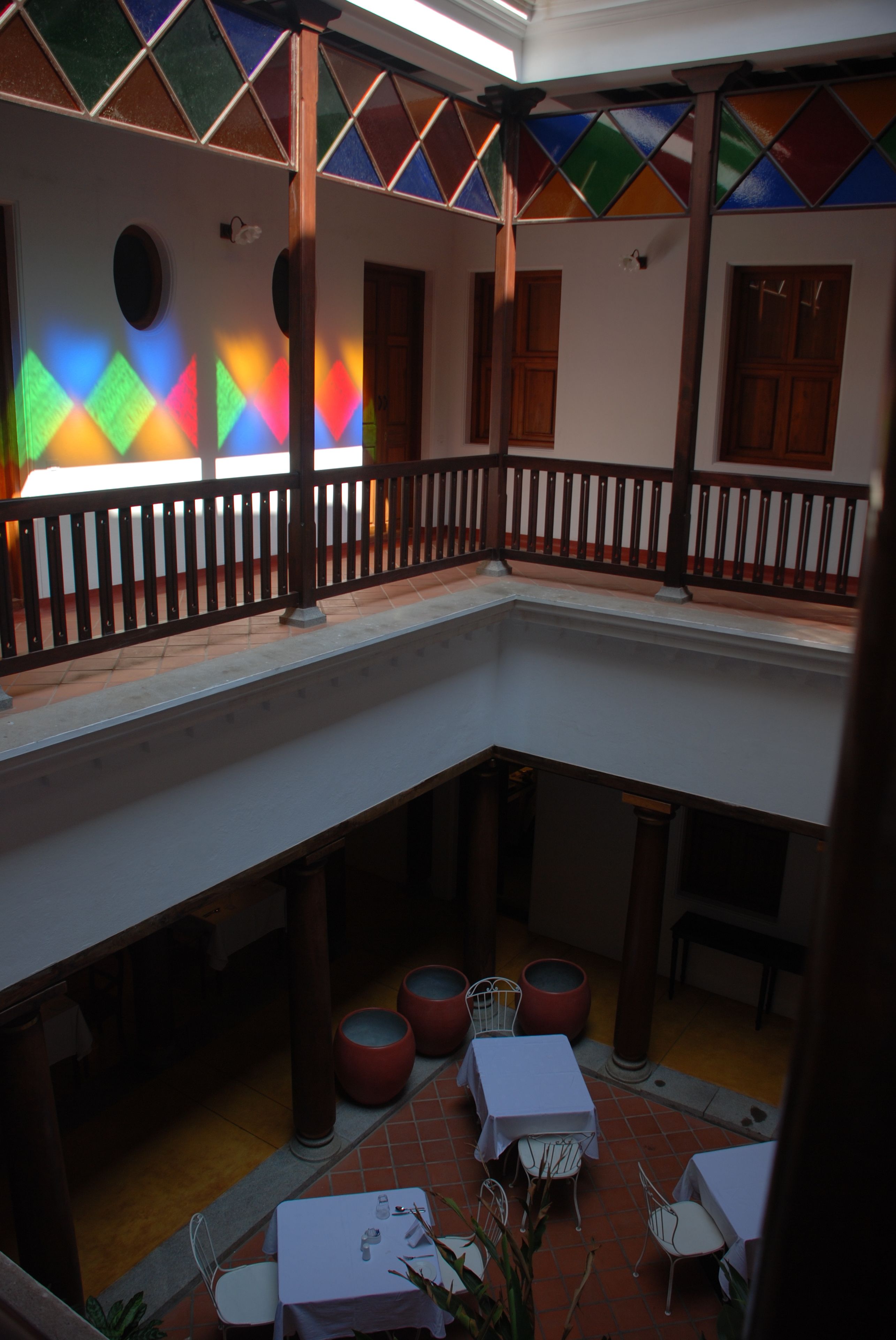 Un patio con balcón, mesas, sillas y una pared de vidrieras de colores.