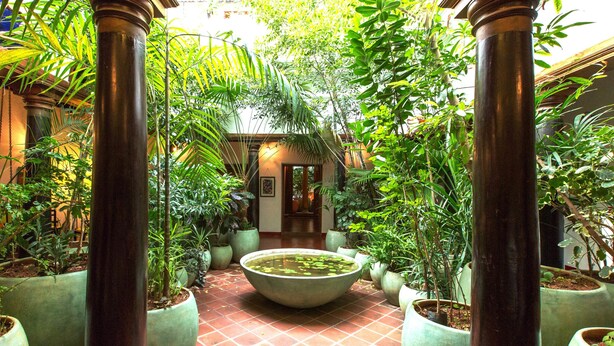 A courtyard with a central water feature surrounded by potted plants and columns. - Maison Perumal - Cgh Earth (Puducherry)