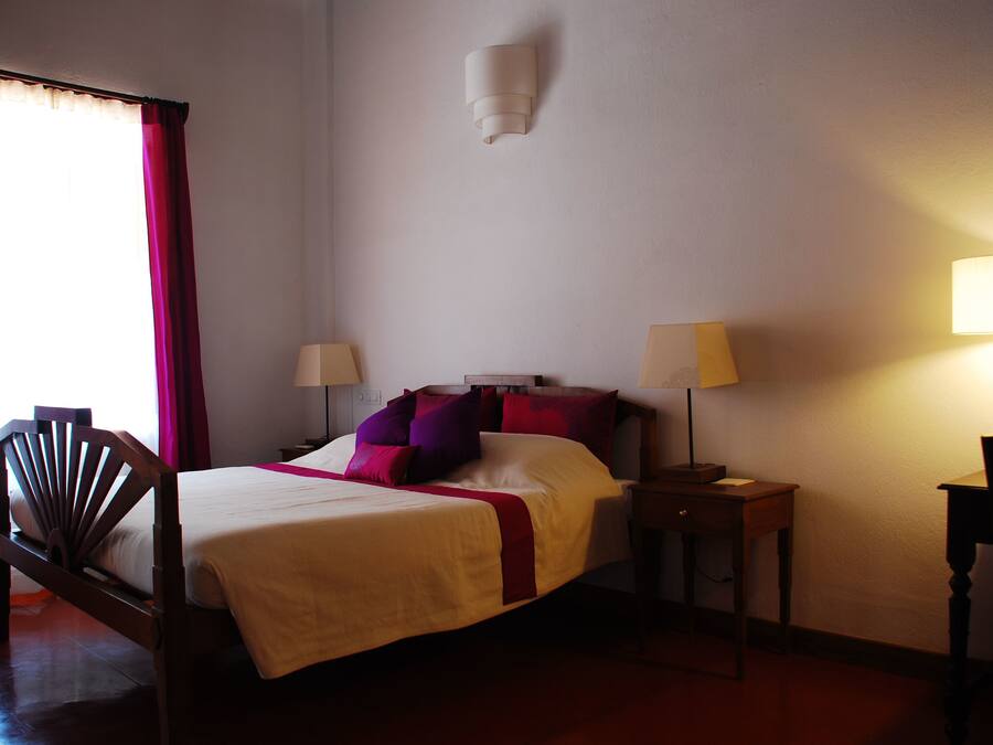 A hotel room with a bed, two bedside tables with lamps, a chair, and a window with curtains.