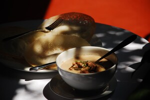 Un tazón de sopa con cuchara y una rebanada de pan sobre un plato.
