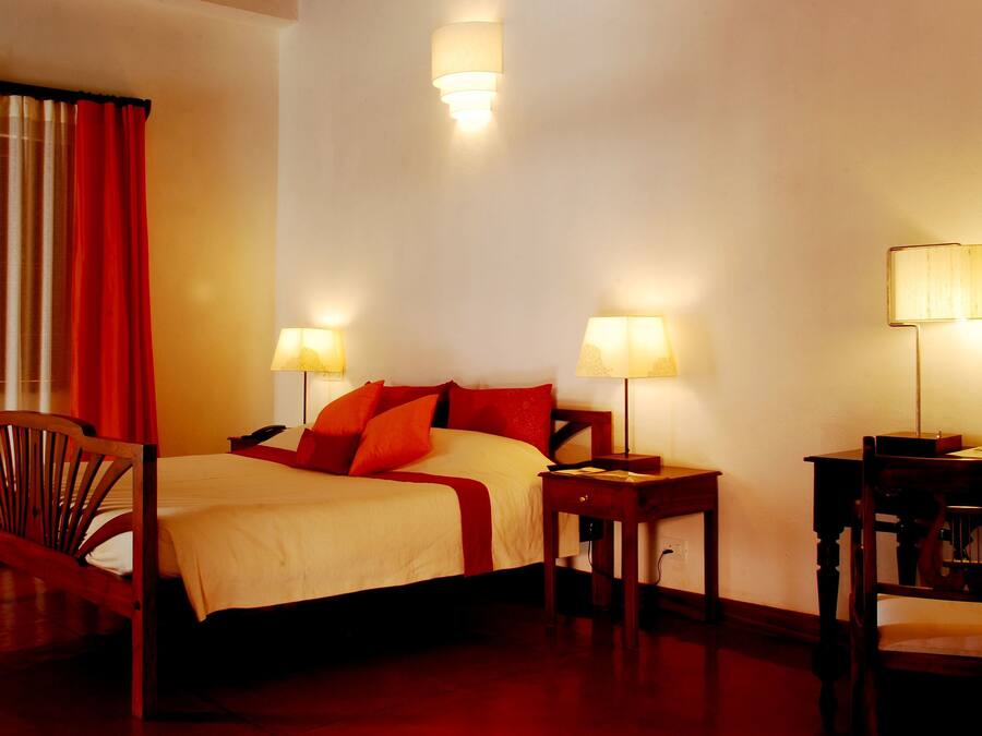 A hotel room with a bed, two bedside tables with lamps, a wooden chair, and a desk with a chair.
