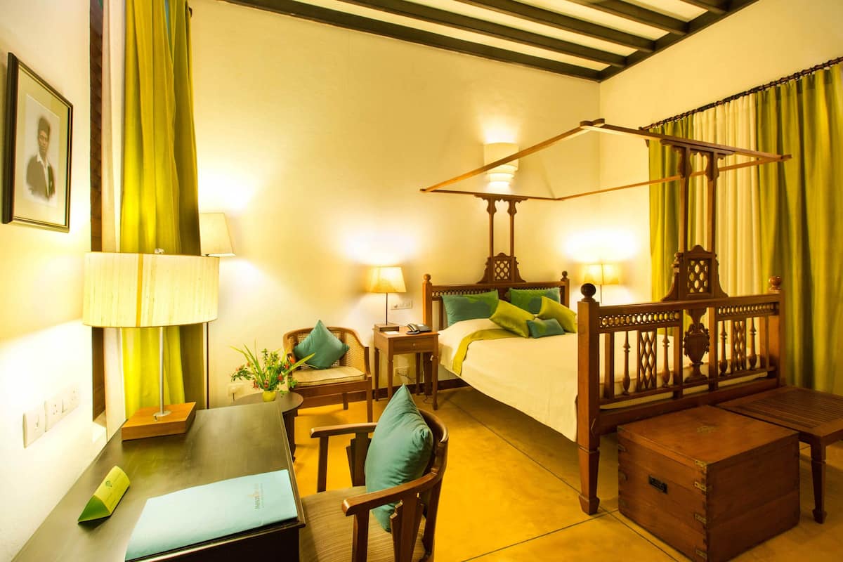 A hotel room with a bed, bedside tables, a desk, a chair, and a wooden chest.