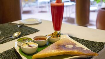 A meal with a triangular-shaped food item, possibly a dosa, accompanied by three small bowls of sauces or dips, and a tall glass of red beverage with a garnish on a white plate.
