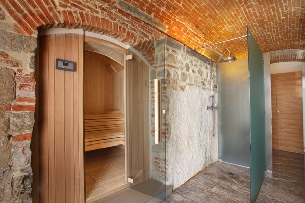 A sauna room with a wooden bench, a glass door, and a stone wall. - Hotel Mulino di Firenze, WorldHotels Crafted (Florence)