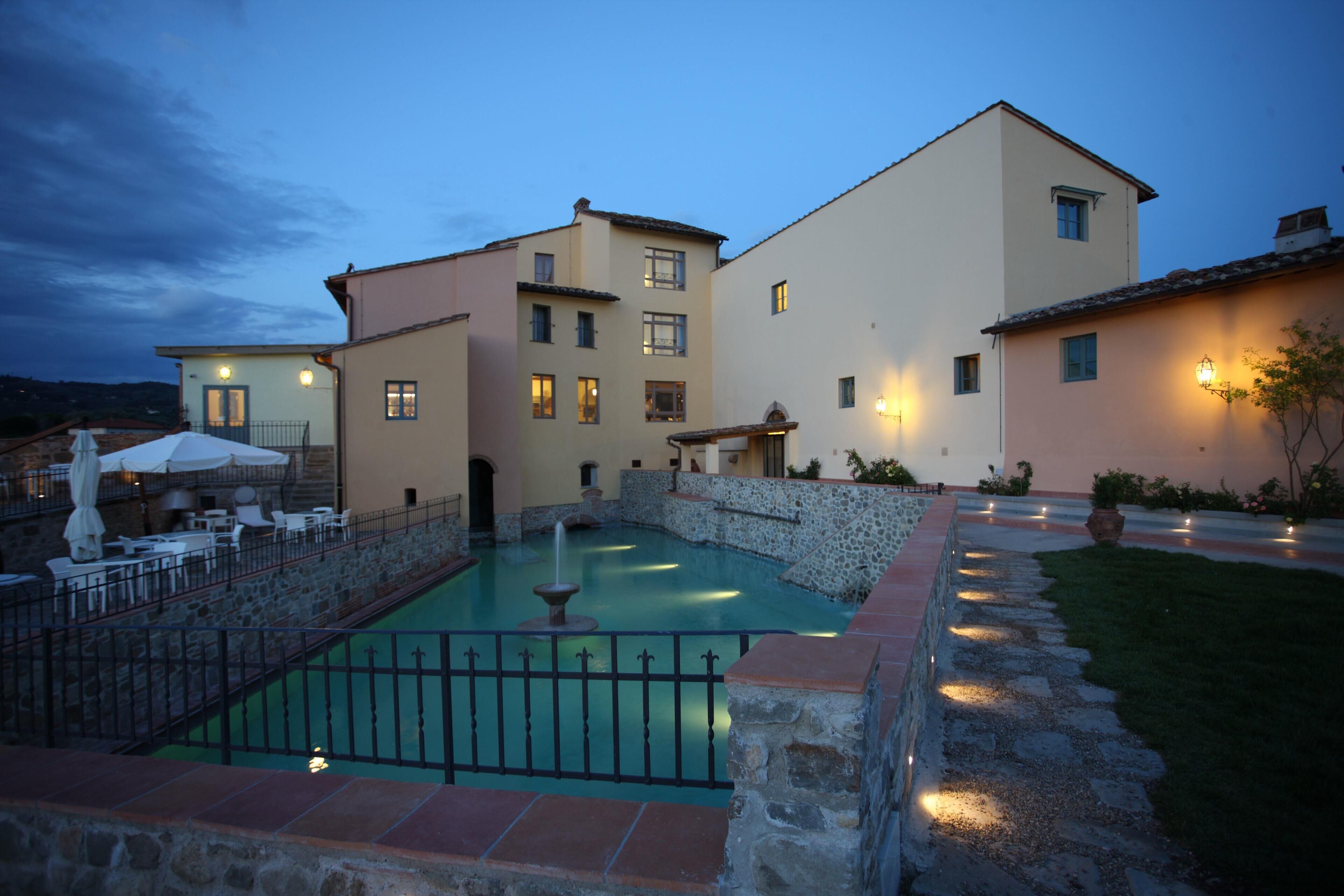 A hotel with a swimming pool, outdoor seating, and a stone wall.