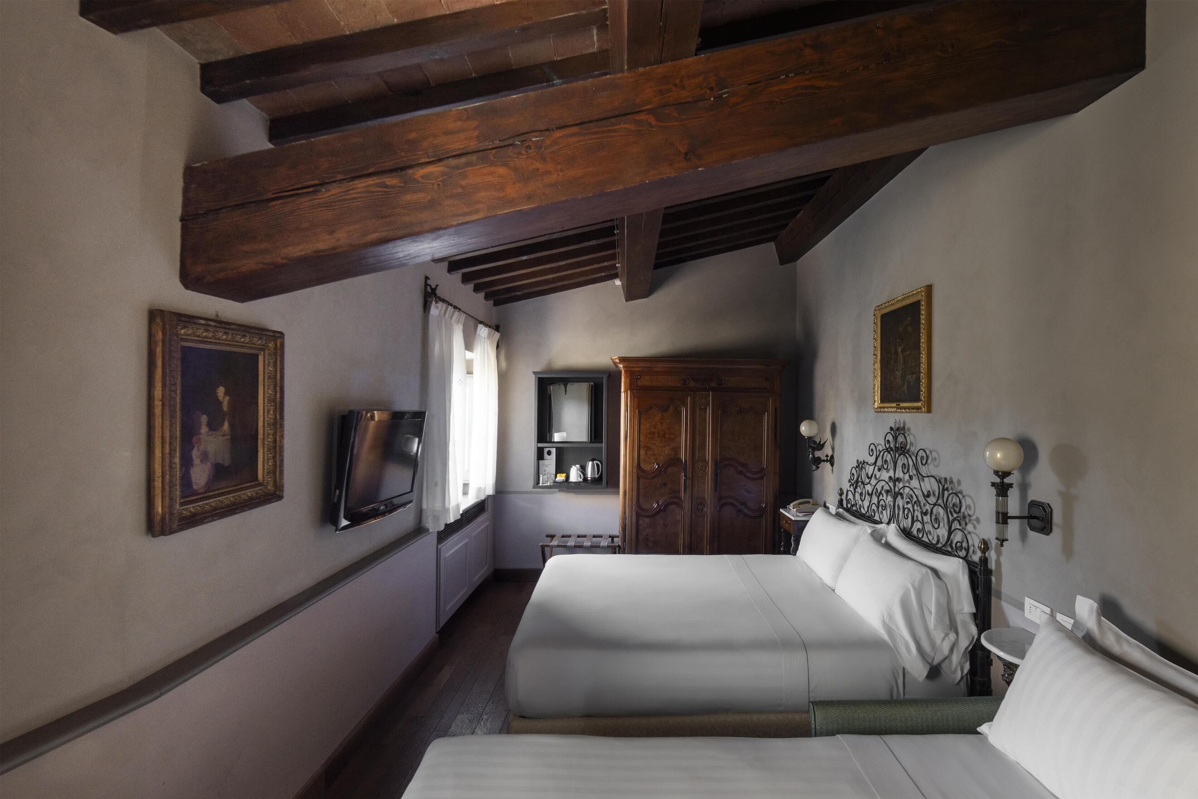 A bedroom with a large bed, wooden ceiling beams, a wardrobe, a television, and a bedside table with a lamp.