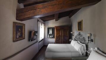 A bedroom with a large bed, wooden ceiling beams, a wardrobe, a television, and a bedside table with a lamp.