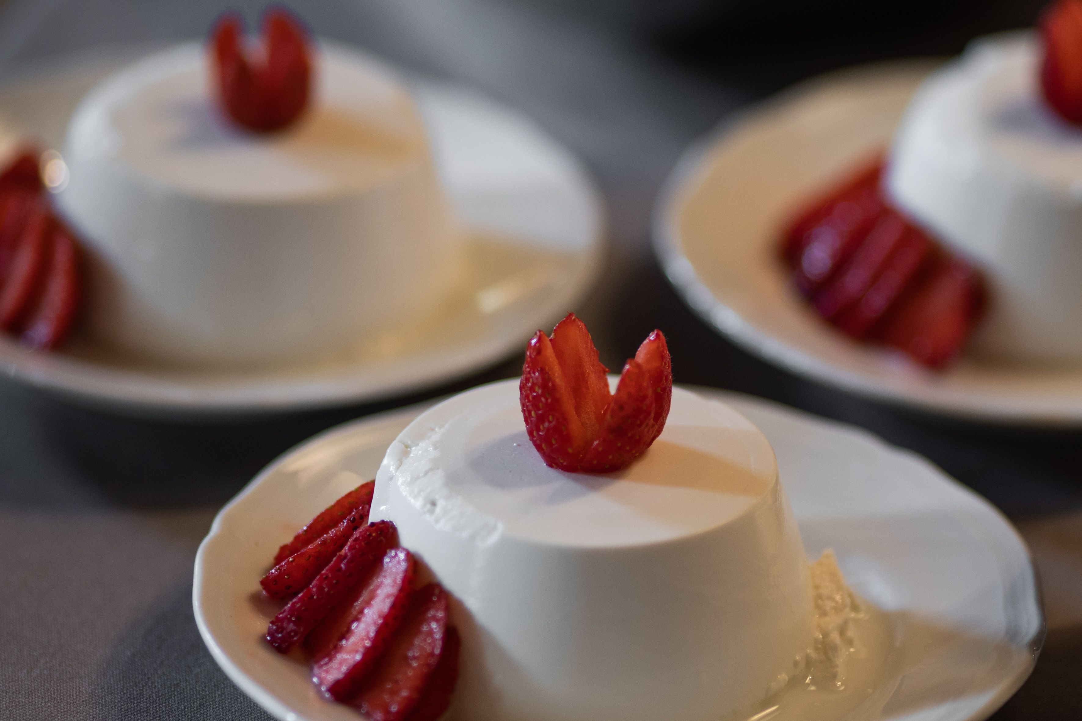 Three white dessert plates with a white dessert and strawberry slices on a table.