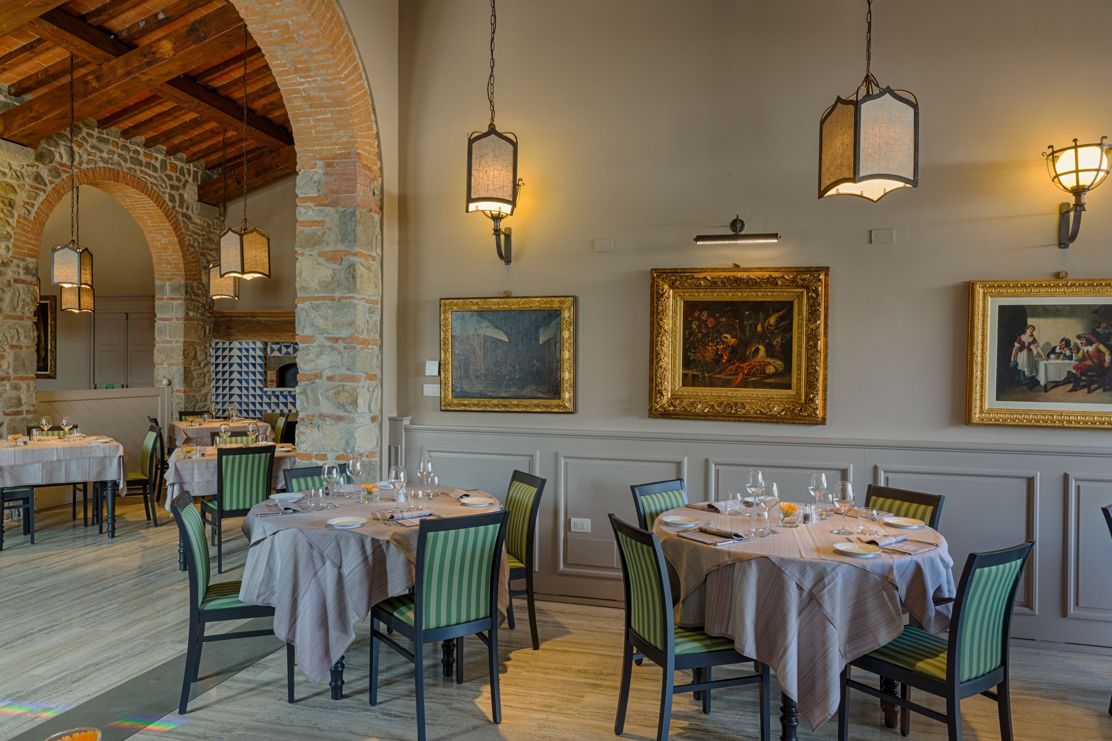 A restaurant with tables set for dining, framed artwork on the walls, and hanging light fixtures.