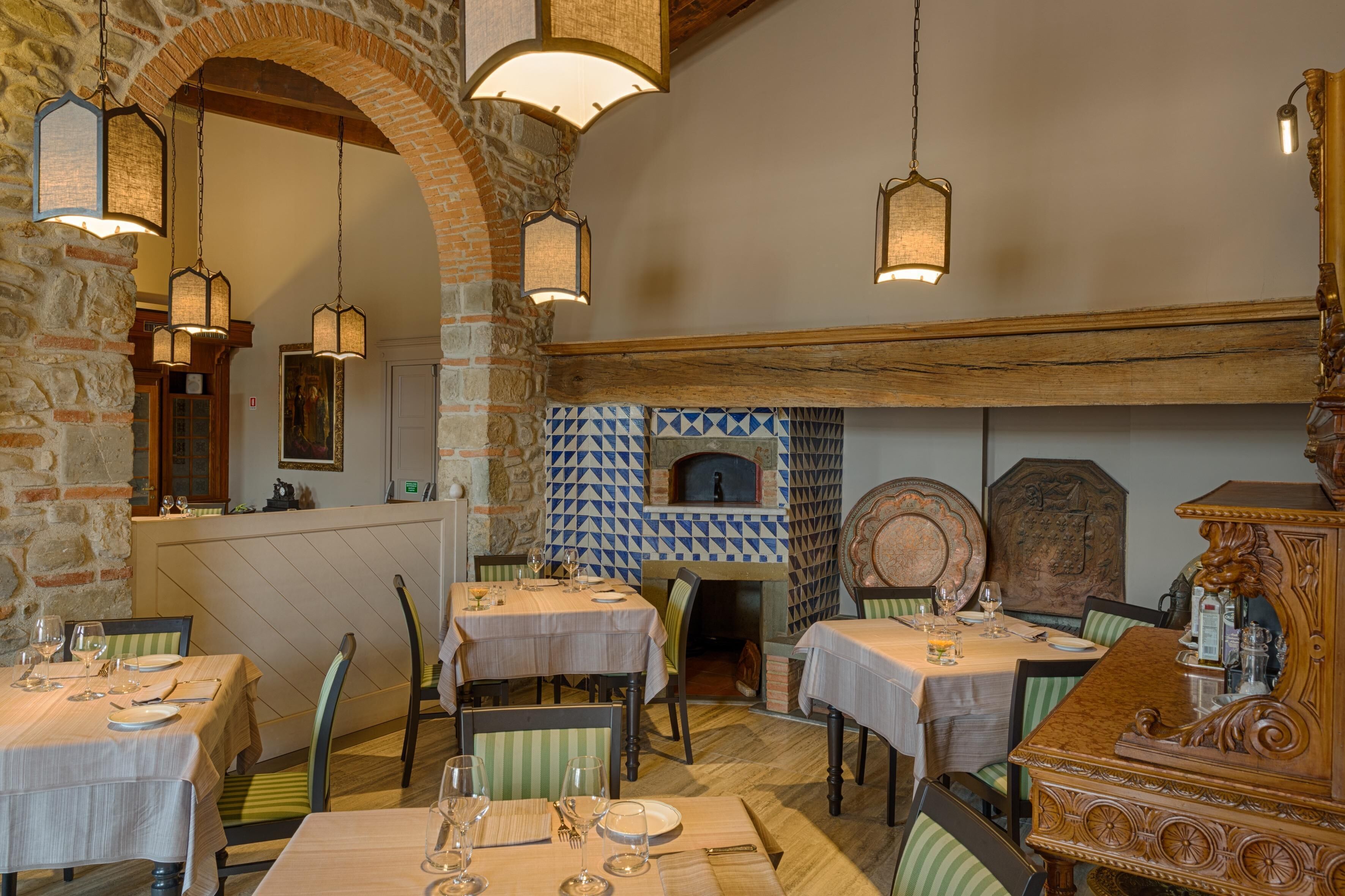 A restaurant with brick walls, wooden beams, and hanging lanterns. Tables are set with white tablecloths and chairs.