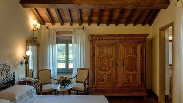 Un dormitorio con una cama, dos sillas, una mesa con flores, un gran armario de madera y un espejo.