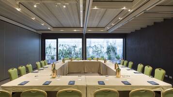 Una sala de conferències amb una taula llarga, cadires verdes i vistes a la vegetació a través de grans finestres.