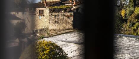 Un edificio de piedra con techo inclinado, rodeado de vegetación y un muro de piedra.