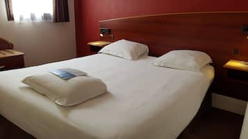 A hotel room with a large bed, two bedside tables, a nightstand, and a window with curtains.