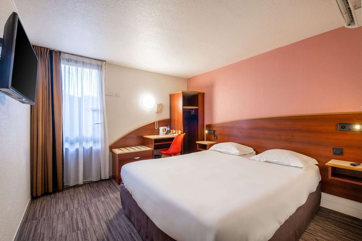 Une chambre d’hôtel équipée d’un lit, d’un bureau, d’une chaise, d’une télévision, d’un téléphone et d’un miroir.
