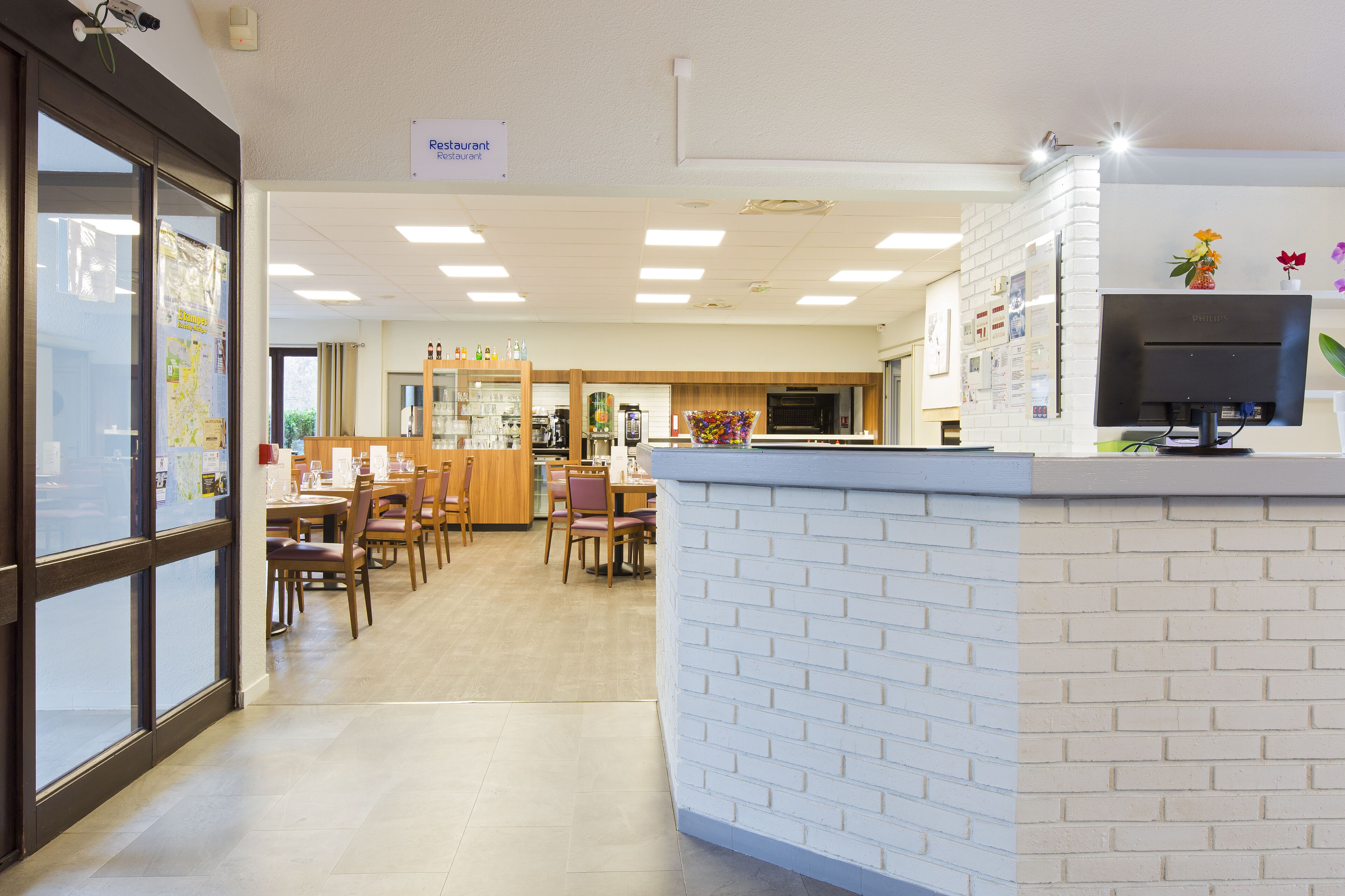 A restaurant with a white brick counter, wooden chairs, and a tiled floor.