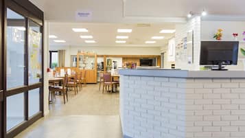 A restaurant with a white brick counter, wooden chairs, and a tiled floor.