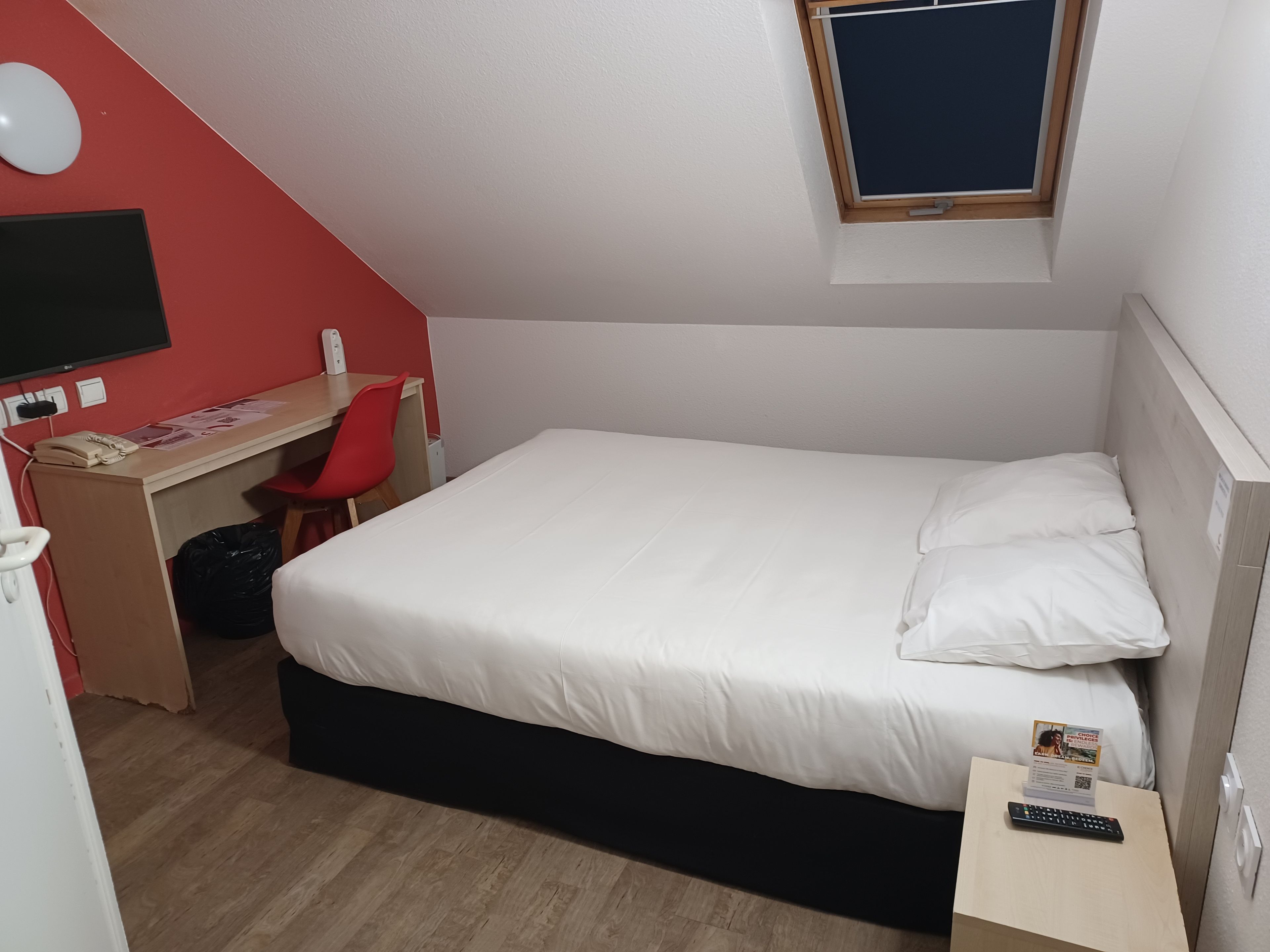 A single-bed room with a desk, chair, and a small window.