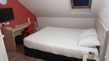 A single-bed room with a desk, chair, and a small window.