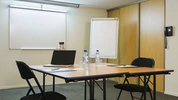 Una sala de conferencias con una mesa, sillas, un ordenador portátil, botellas de agua, una pizarra y un teléfono.