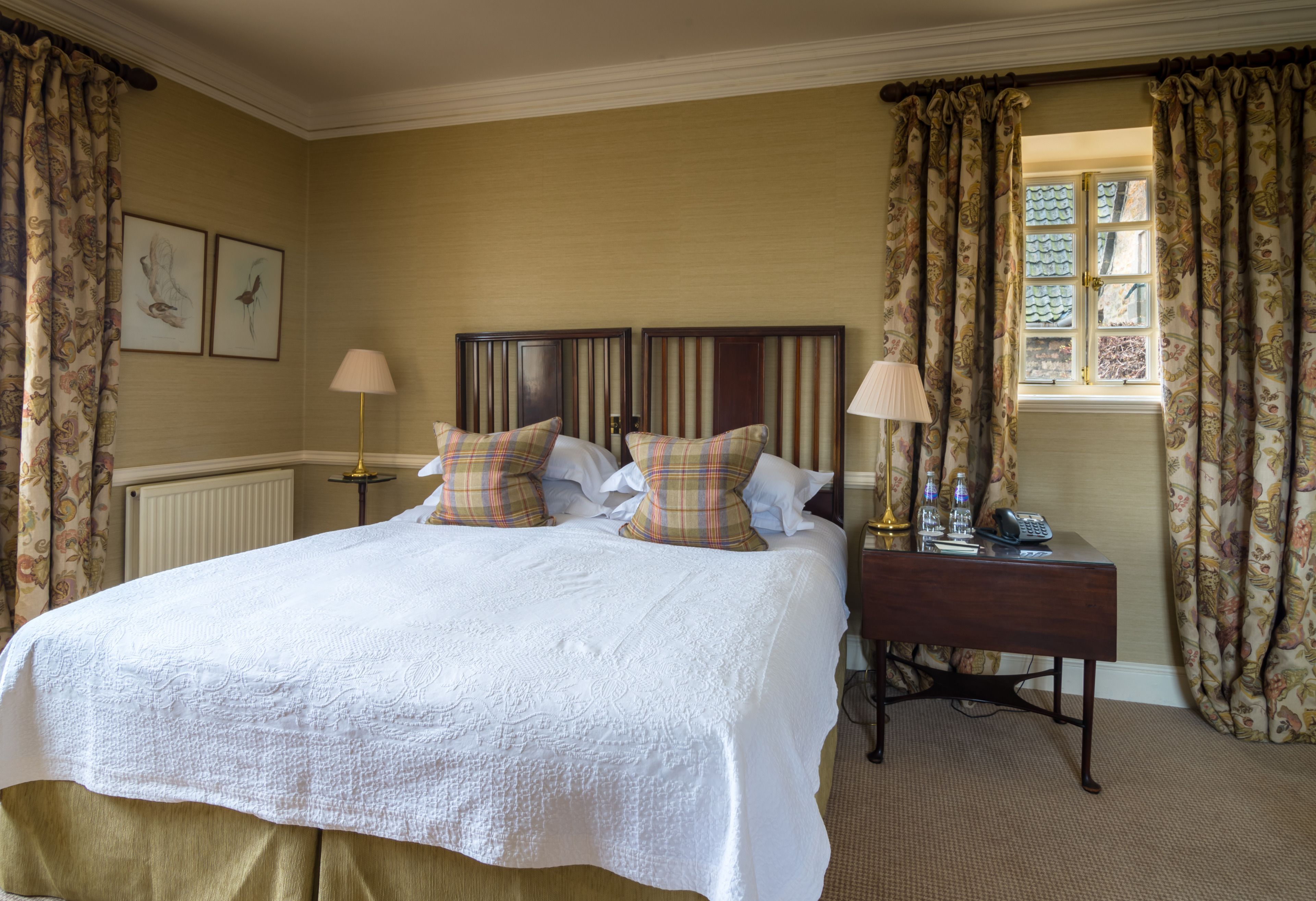 A hotel room with a large bed, two bedside lamps, a nightstand, and a window with curtains.