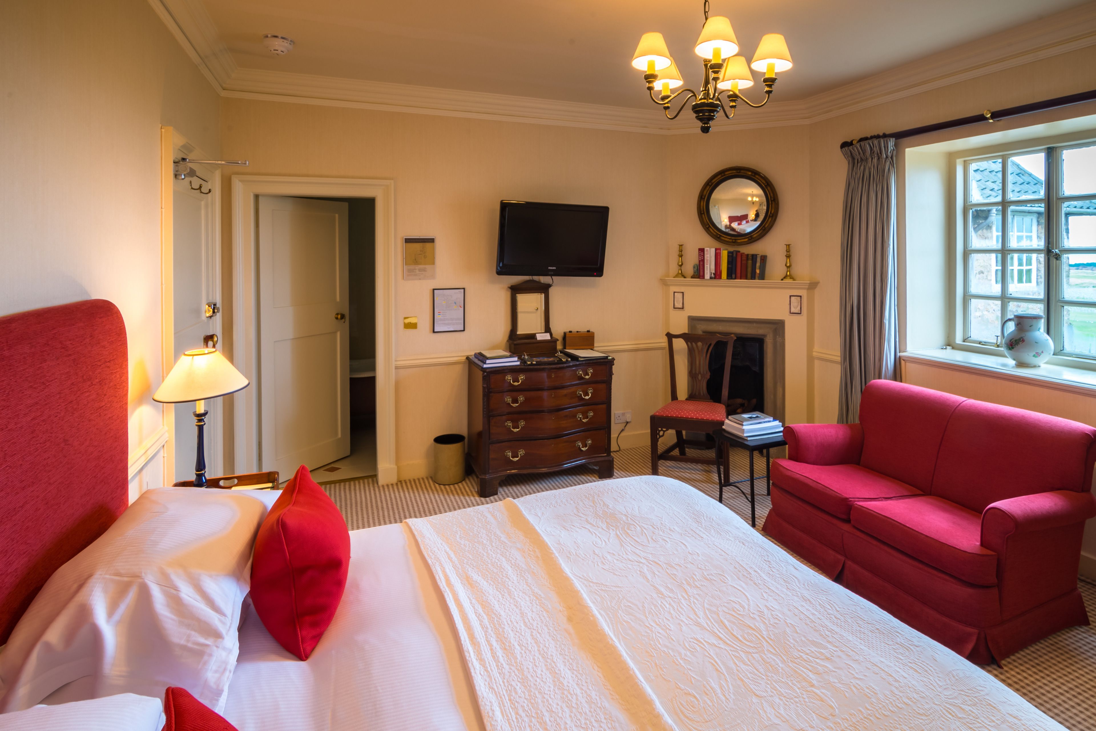 Una habitación de hotel con una cama, un sillón rojo, un televisor, una chimenea y una ventana con vistas.