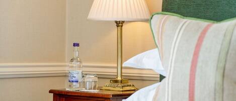 A neatly made bed with a green-striped pillow, a bedside table with a lamp, and a bottle of water.
