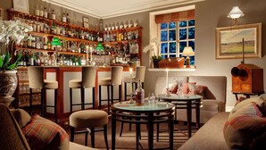 A bar area with shelves of liquor bottles, a bar counter, and seating with a view of the outdoors. - Greywalls Hotel and Chez Roux (Gullane)