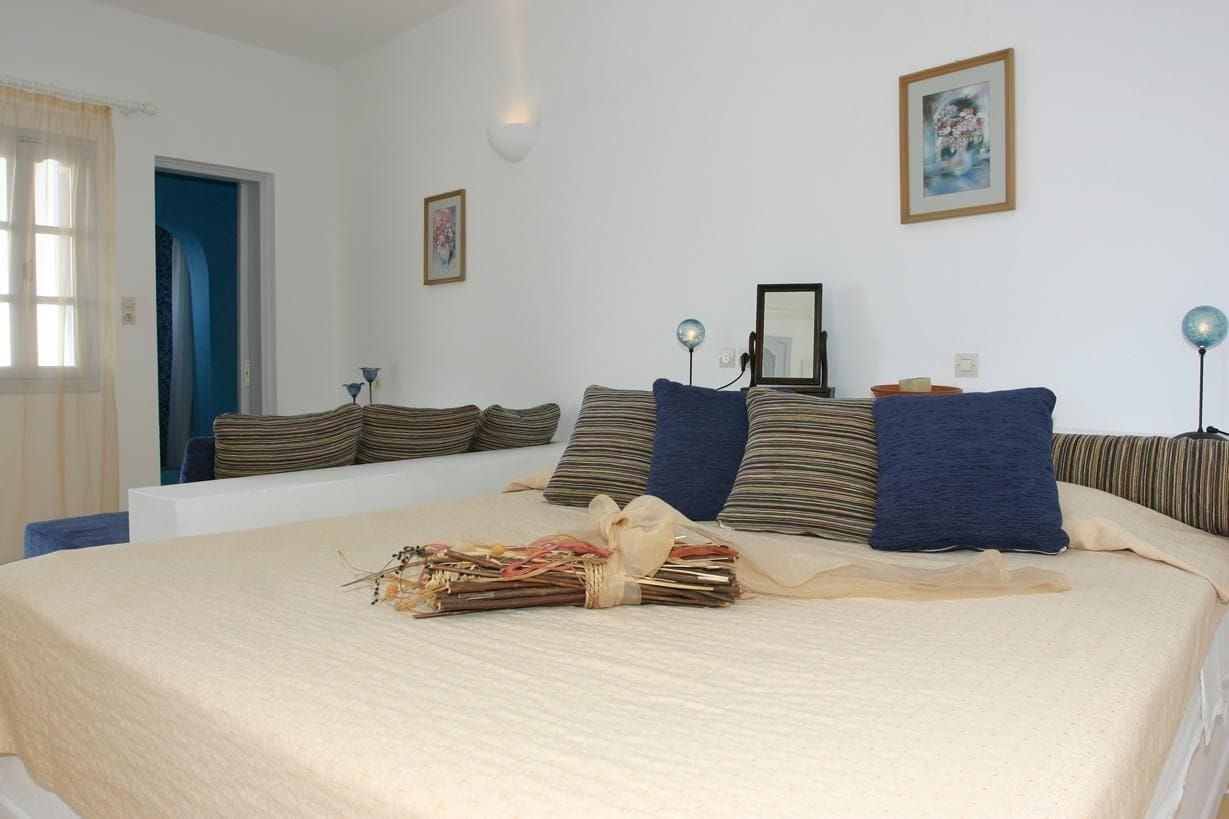 Un dormitorio con una cama grande, almohadas a rayas, una mesita de noche, una lámpara y un cuadro enmarcado en la pared.