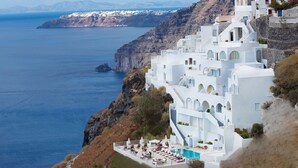 A white building with a pool and outdoor seating, overlooking the sea. - Tzekos Villas (Santorini)