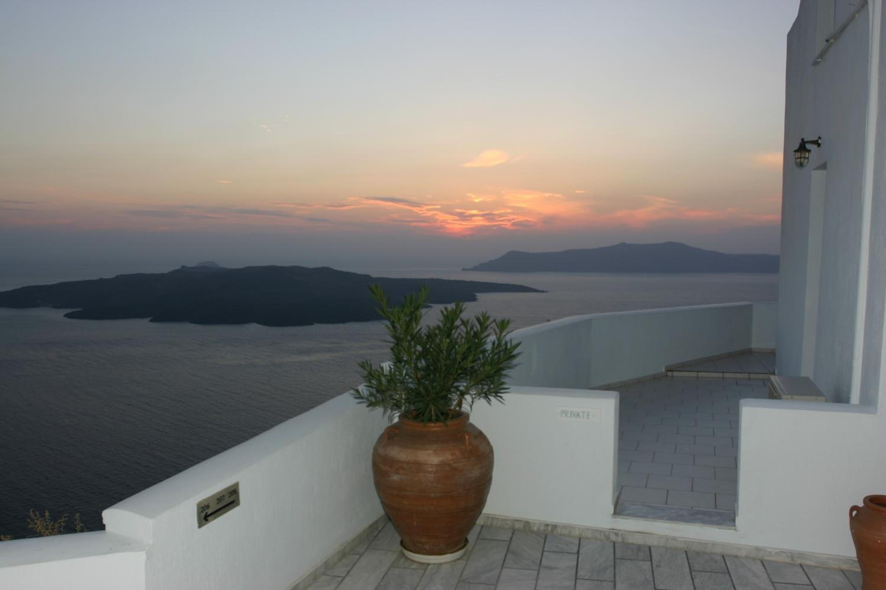 A terrace with a view of the sea and islands, a large terracotta pot, and a sign indicating 'PRIVATE'.