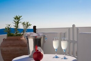 A table with a potted plant, a thermos, a red apple, and two glasses of white beverage on a terrace with a clear sky. - Tzekos Villas (Santorini)