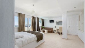 A modern hotel room with a large bed, a desk, a sofa, and a TV. - Tzekos Villas (Santorini)