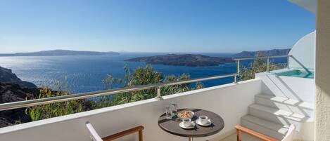 A balcony with a table and chairs, overlooking a coastal view with the sea and distant land.