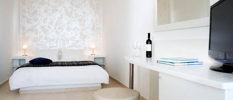 A modern hotel room with a bed, a desk with a computer, a wine bottle, and glasses.