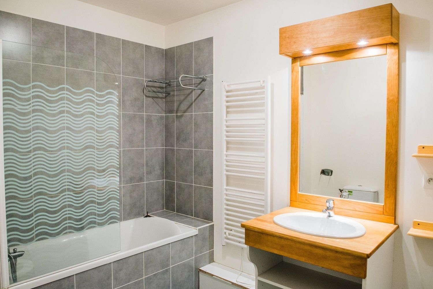 A bathroom with a bathtub, a wooden vanity with a sink, and a mirror with a wooden frame.