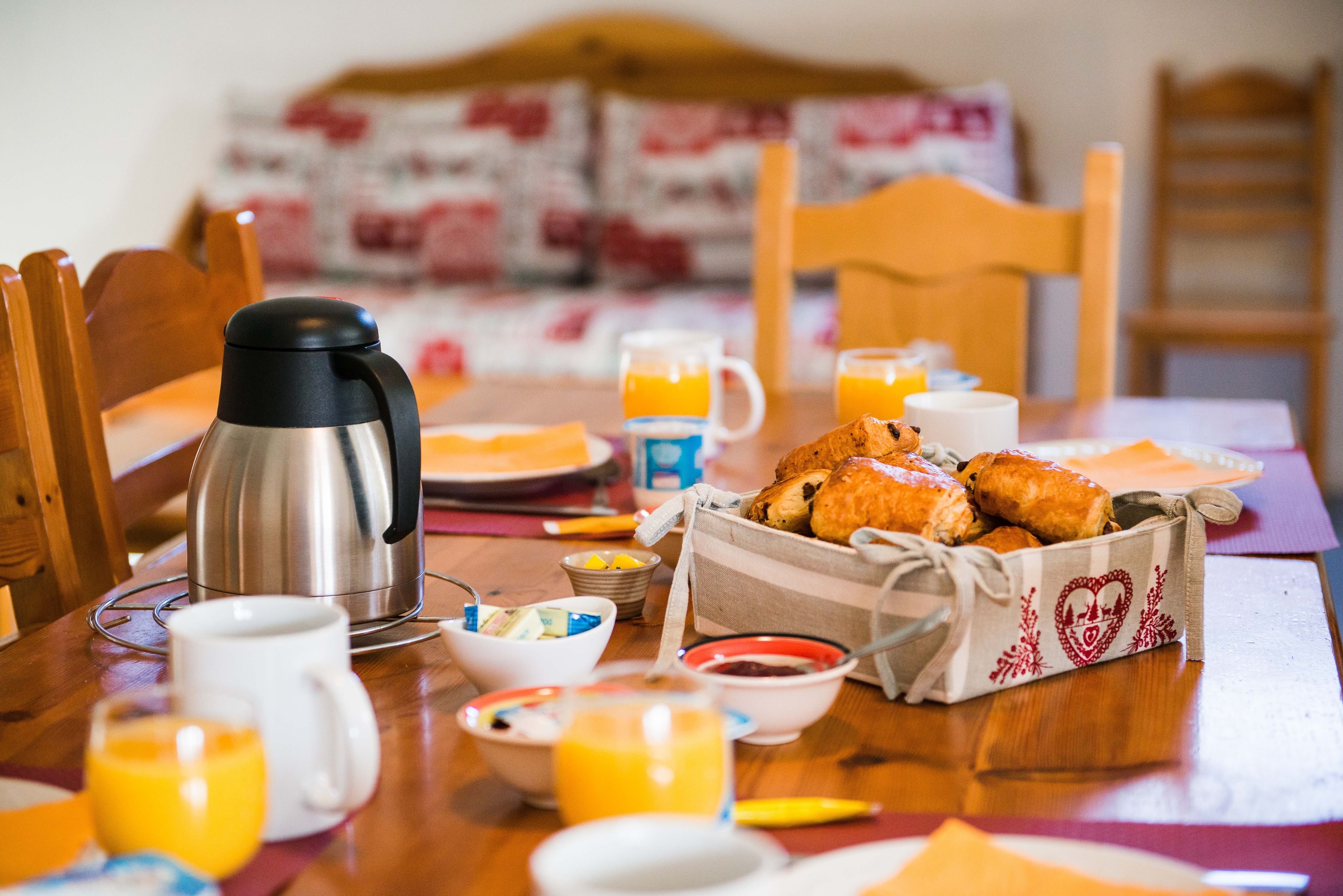 A breakfast table with a coffee maker, croissants, orange juice, and various breakfast items.