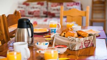 A breakfast table with a coffee maker, croissants, orange juice, and various breakfast items.