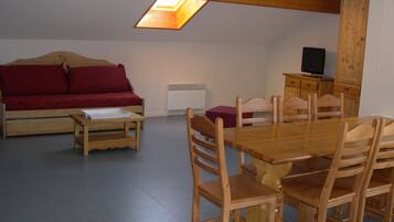 Een kamer met een houten eettafel, houten stoelen, een rode bank, een kleine houten tafel en een televisie op een houten kast.