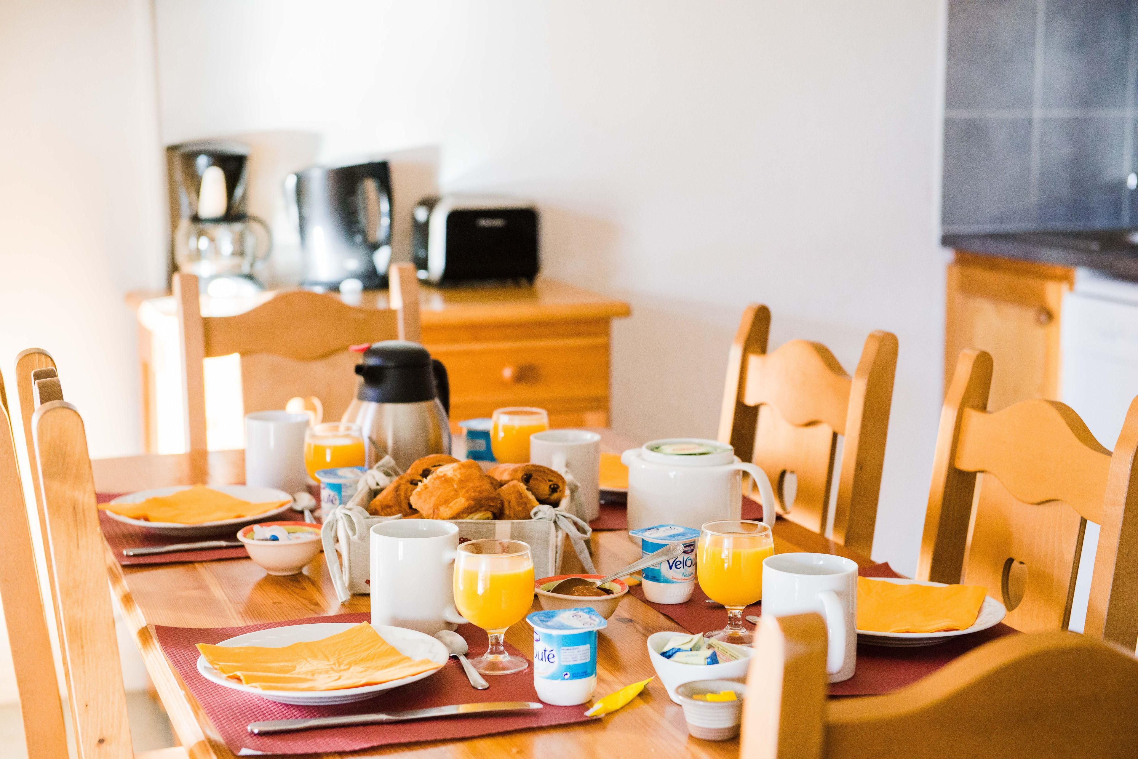 A breakfast table set with plates, bowls, cups, and a coffee maker.