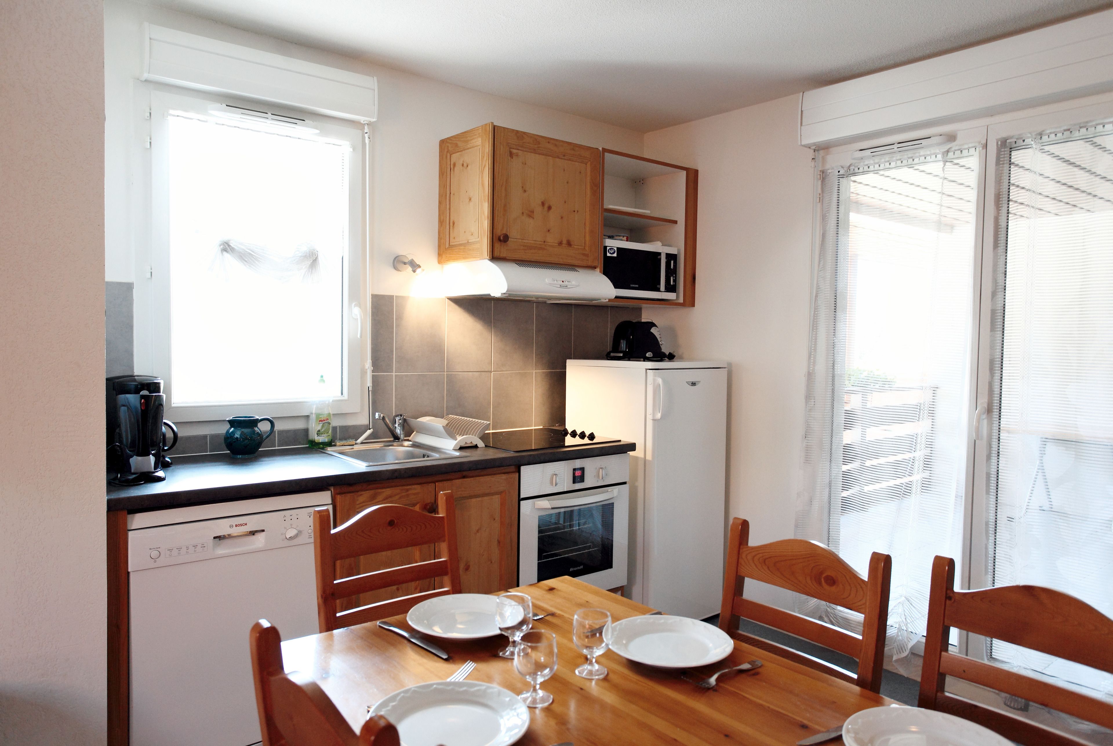 A compact kitchen with wooden cabinets, a microwave, a dishwasher, and a dining table set for four.
